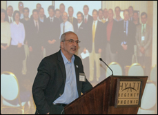 Murray Fingeret speaking at the Optometric Glaucoma Society meeting with a picture of the initial meeting group in 2001 in the background.