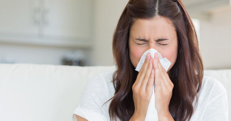 woman sneezing into tissue or blowing her nose