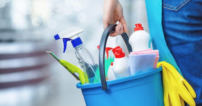 Woman holding a bucket of cleaning products.