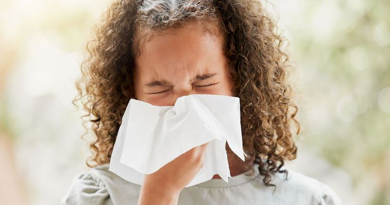 Girl blowing her nose and looking uncomfortable.