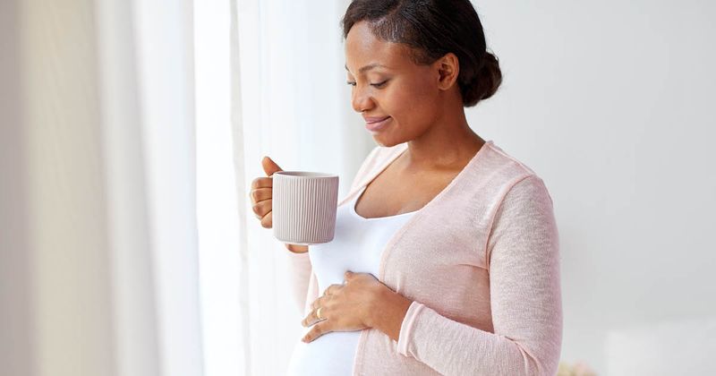 Happy pregnant women with cup drinking tea at home.