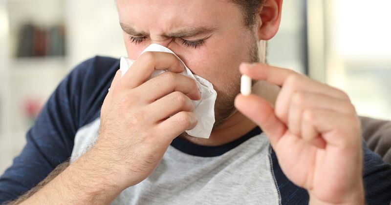 Man blowing his nose and holding a pill