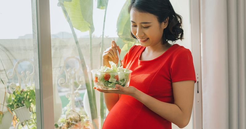 Pregnant Asian woman eating a salad. 