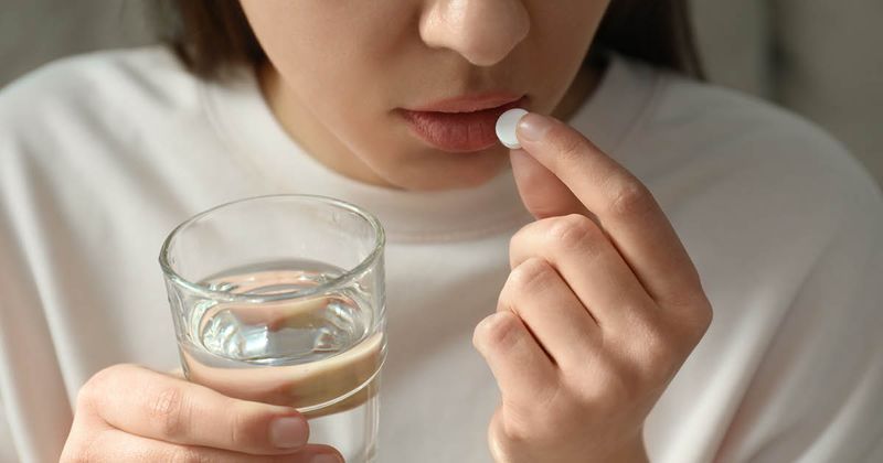 Woman taking a white pill and holding a glass of water