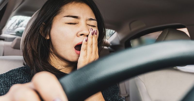 Young Asian woman yawning while sitting behind a steering wheel