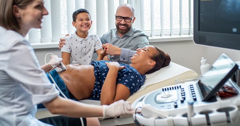 Image of a pregnant woman with her family as an ultrasound takes place 