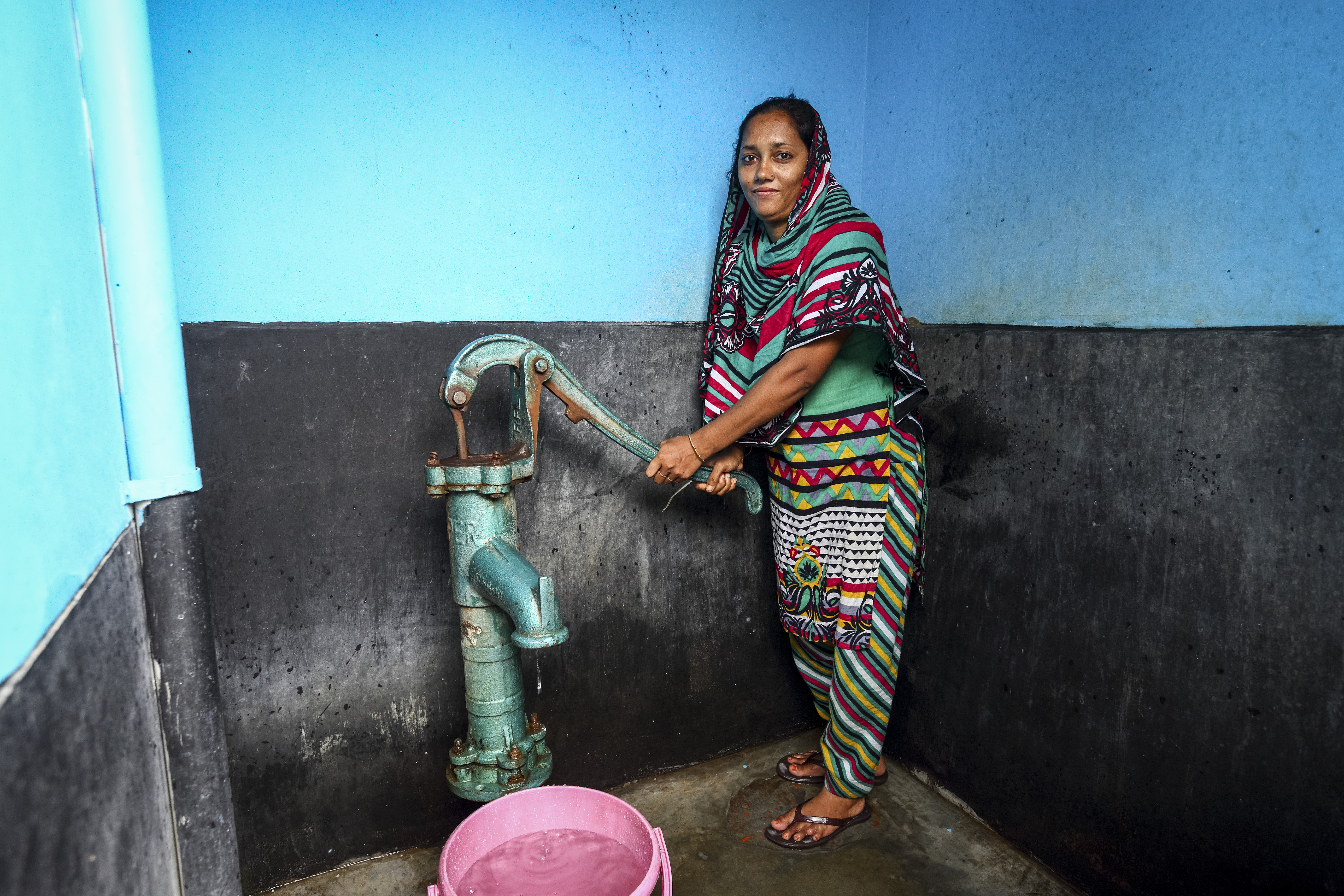 A woman pumps water from a shared community tap in Dhaka, Bangladesh