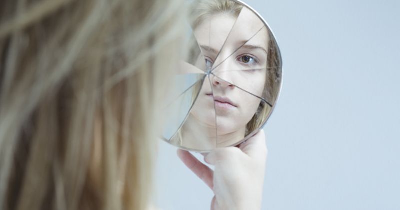 Woman looking into broken glass mirror.