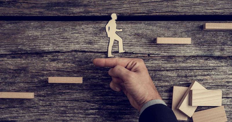 Businessman supporting paper cut out of a man climbing stairs.