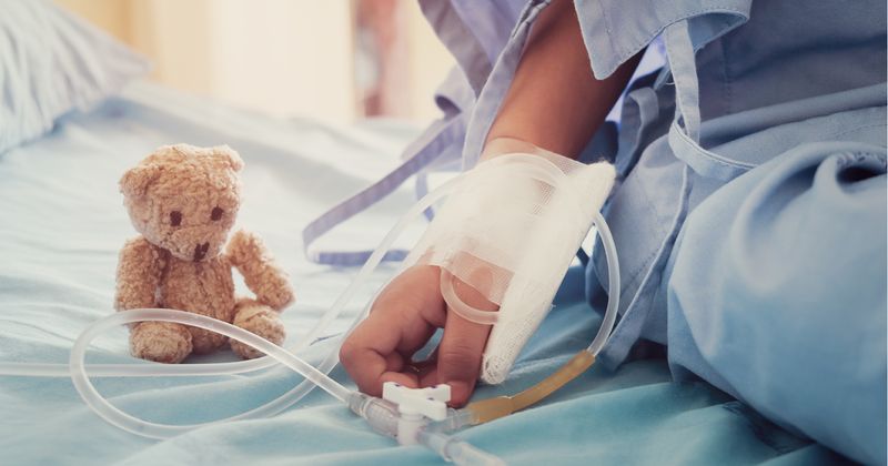 Arm of child on hospital bed with teddy bear