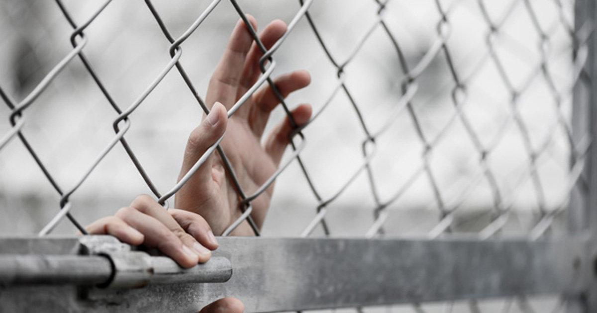 Photo of a migrant child in detention grabbing chain link fence