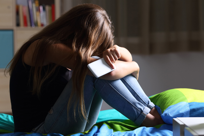 Depressed teenage girl in bedroom on phone crying