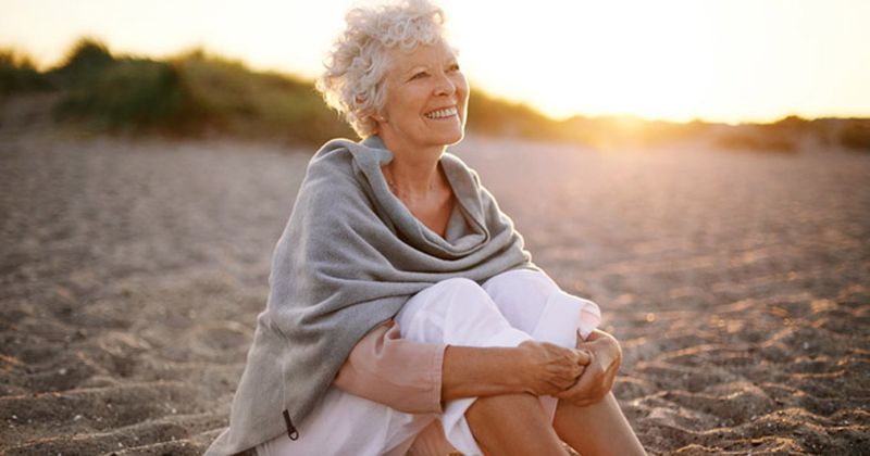 happy older woman sits on a beach