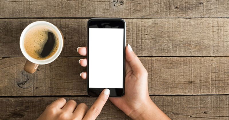 phone in person's hands next to cup of coffee