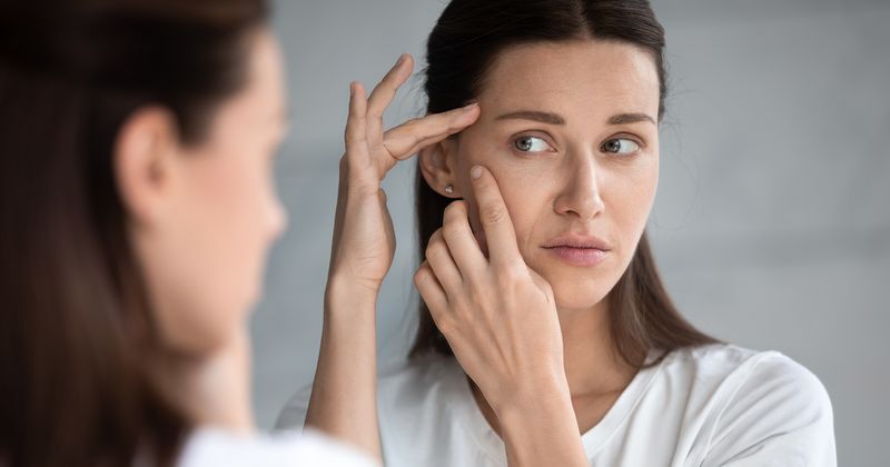 Woman looking in mirror worried about wrinkles.