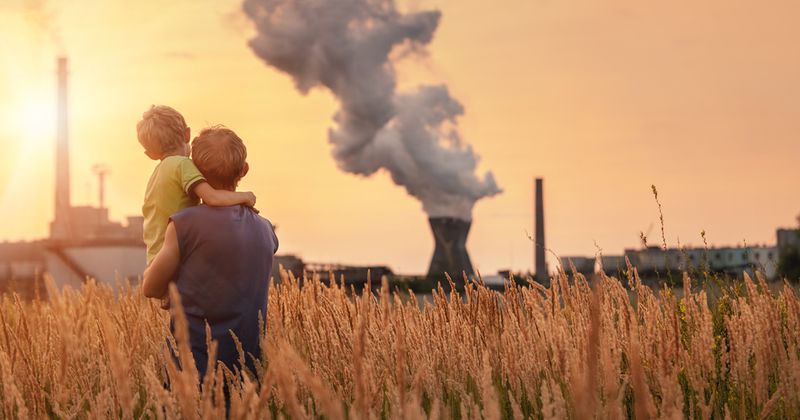 Parent holding child while looking at air pollution from a factory.