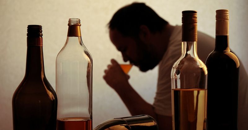 Silhouette of person drinking behind bottles of alcohol