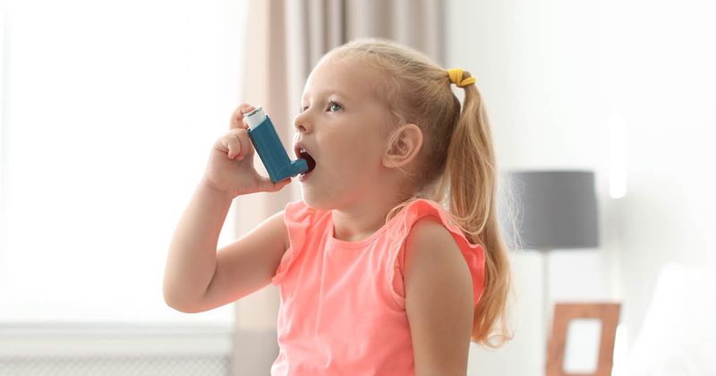 Little girl using an asthma inhaler in bedroom.