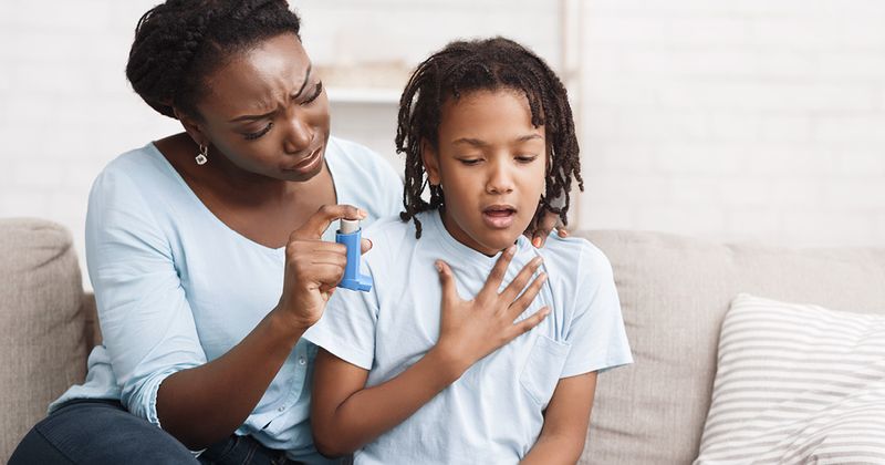 Black mother holding asthma inhaler for daughter.