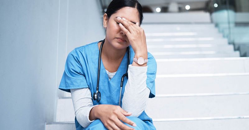 Female nurse looking stressed while sitting on a staircase.