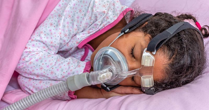 Child suffering from sleep apnea using a CPAP machine.