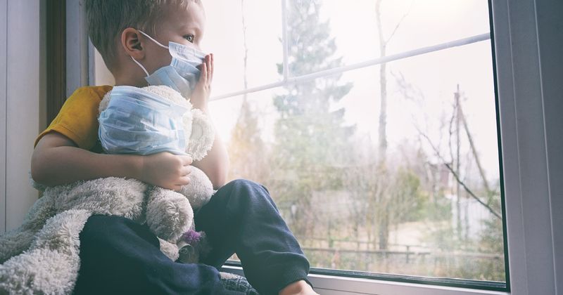 Child wearing mask looking out a window.