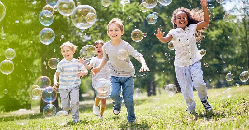 A group of children smiling and running though bubbles on a sunny day.