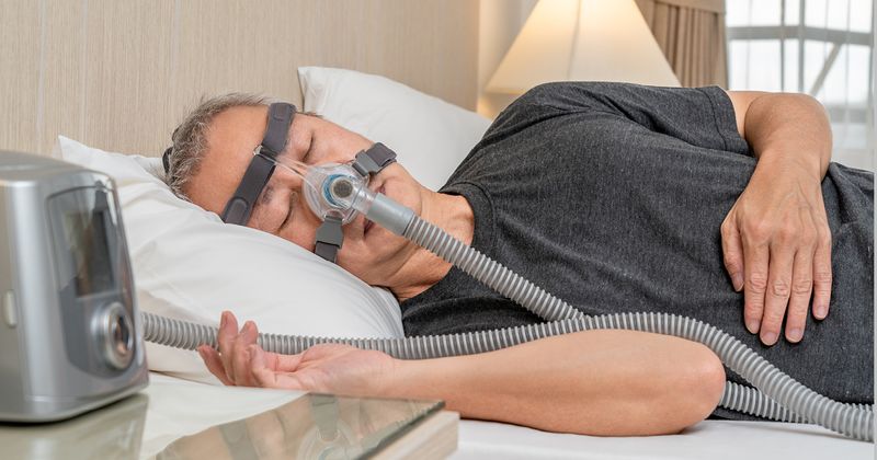 Older man with sleep apnea wearing CPAP headgear and mask while sleeping.