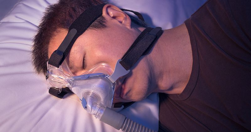 Asian man with sleep apnea using CPAP machine.