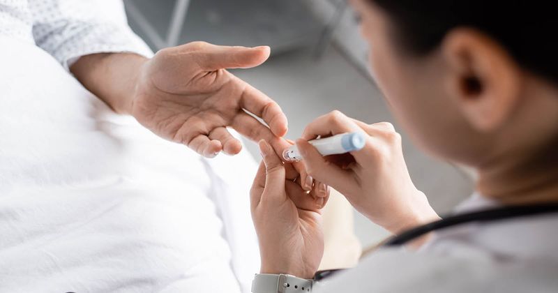 Doctor holding lancet pen near hand of patient with diabetes in hospital.