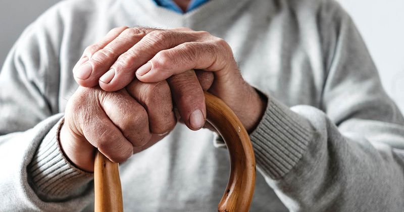 Hands of an older man resting on a walking cane.