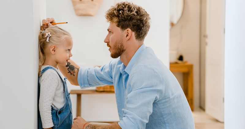 Father measuring height of daughter at home.