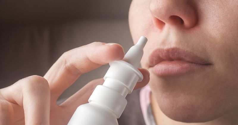 Woman holding nasal spray by her nose.