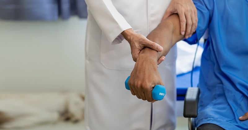 Physiotherapist treating hospital patient, who is lifting a weight.