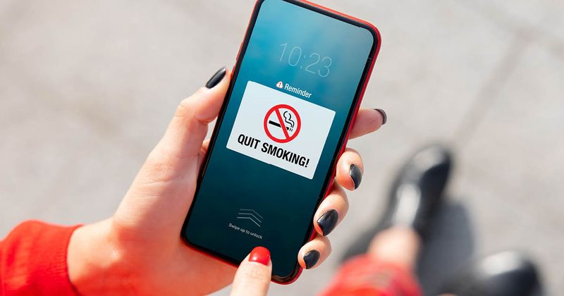 Woman holding a mobile phone and looking at a notification reminding her to quit smoking.