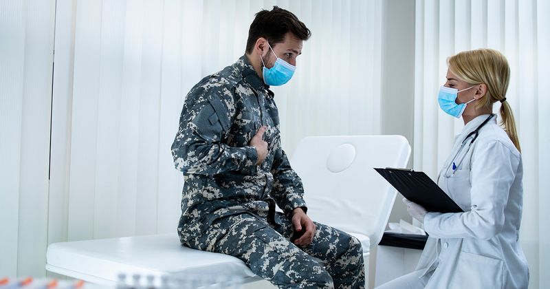 Soldier in uniform with face mask complaining about chest pains to doctor.