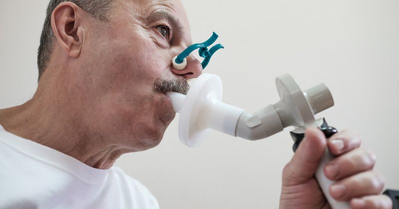 Hispanic man testing breathing function by spirometry.