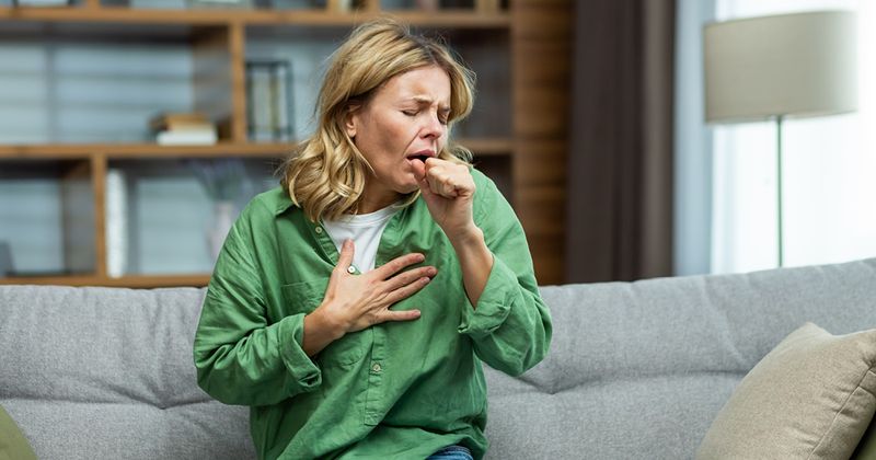 Woman sitting down on couch coughing into hand