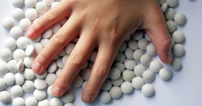 Caucasian hand hovering over white pills on white table