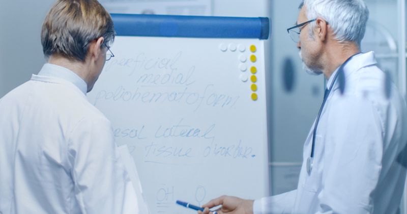 Two male doctors standing, facing a white board