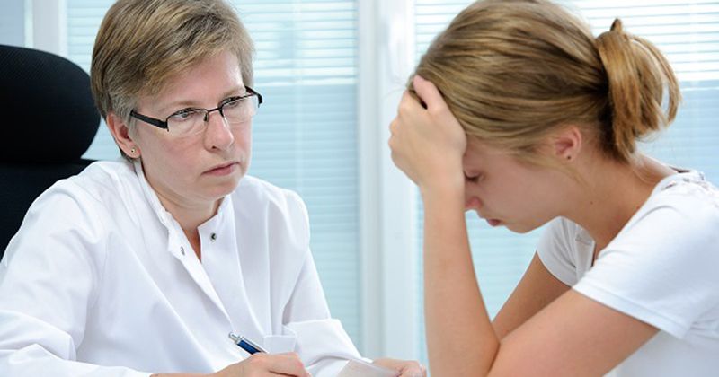 Two women in office setting, one listening, one appearing unwell.