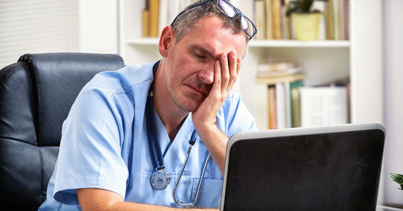 Man sitting in chair looking at laptop and tired.