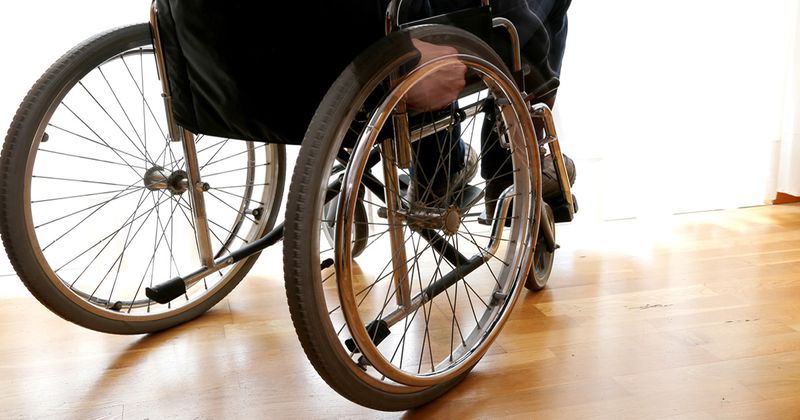 Person putting hand on wheel of wheelchair from rear view